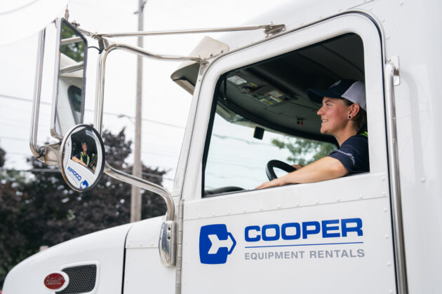 Woman driving a large transportation truck. She smiles at the camera.