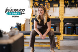 A blonde woman smiles and sits in a warehouse.